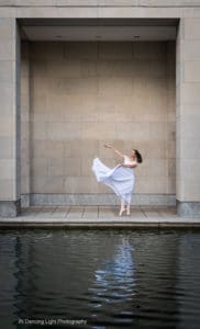 Ballet dancer framed by the buildings columns with her reflection in the water