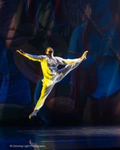 A dancer wearing a simple white kurta leaps into the air.
