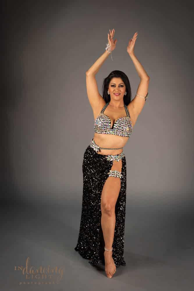 Mediterranean belly dancer in a jeweled costume with lifted arms