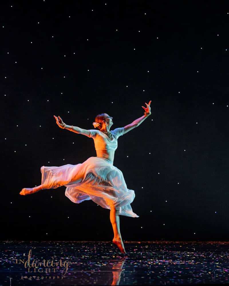 Female dancer leaps into the air against a stary background.