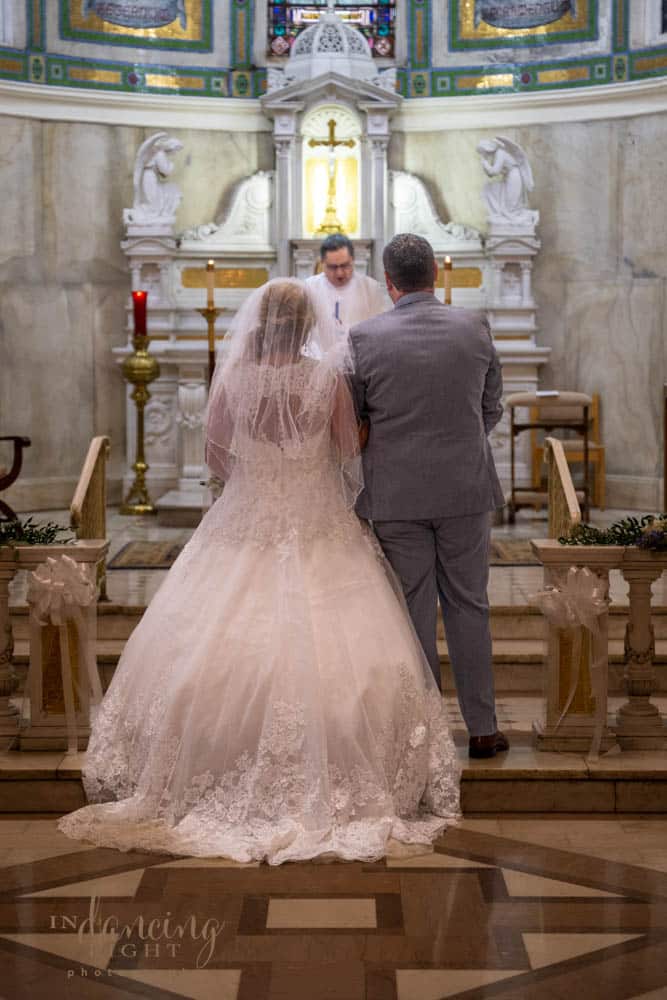 Bride and groom stand facing the front of the chapel during their wedding in the Indianapolis Cathedral.