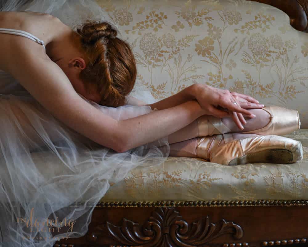 Ballet dancer with pointe shoes stretches on a sofa