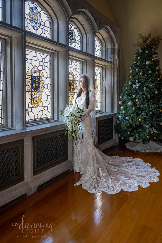 Bride in a beautiful gown holds her bouquet of white lilies as she stands by a window in Indianapolis Laurel Hall