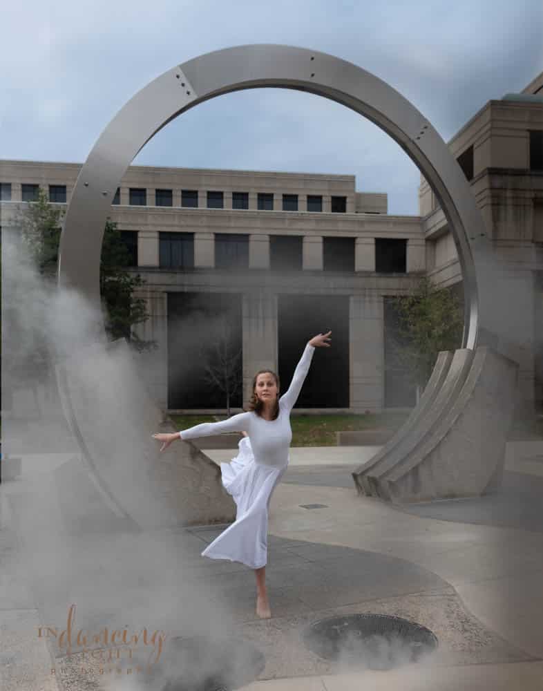 Ballerina dances in front of a circular sculpture as steam rises around her
