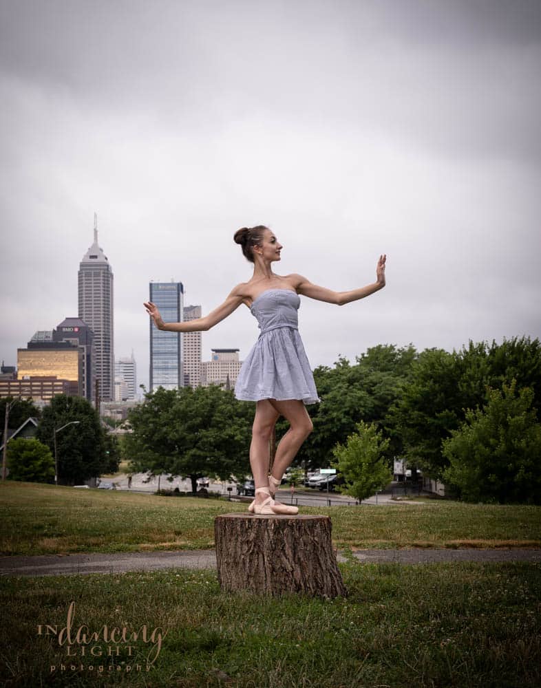A ballerina dances on a stump with the Indianapolis skyline in the background