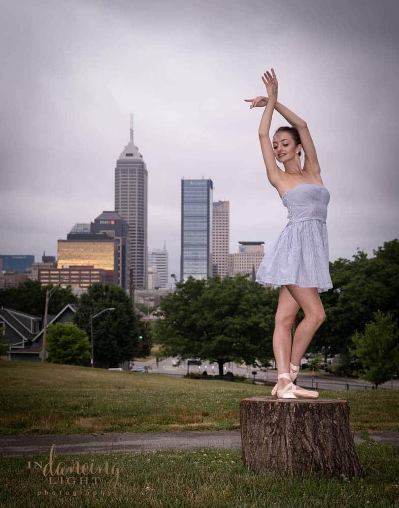 Ballet dancer standing on a tree stump with the Indianapolis skyline in the background