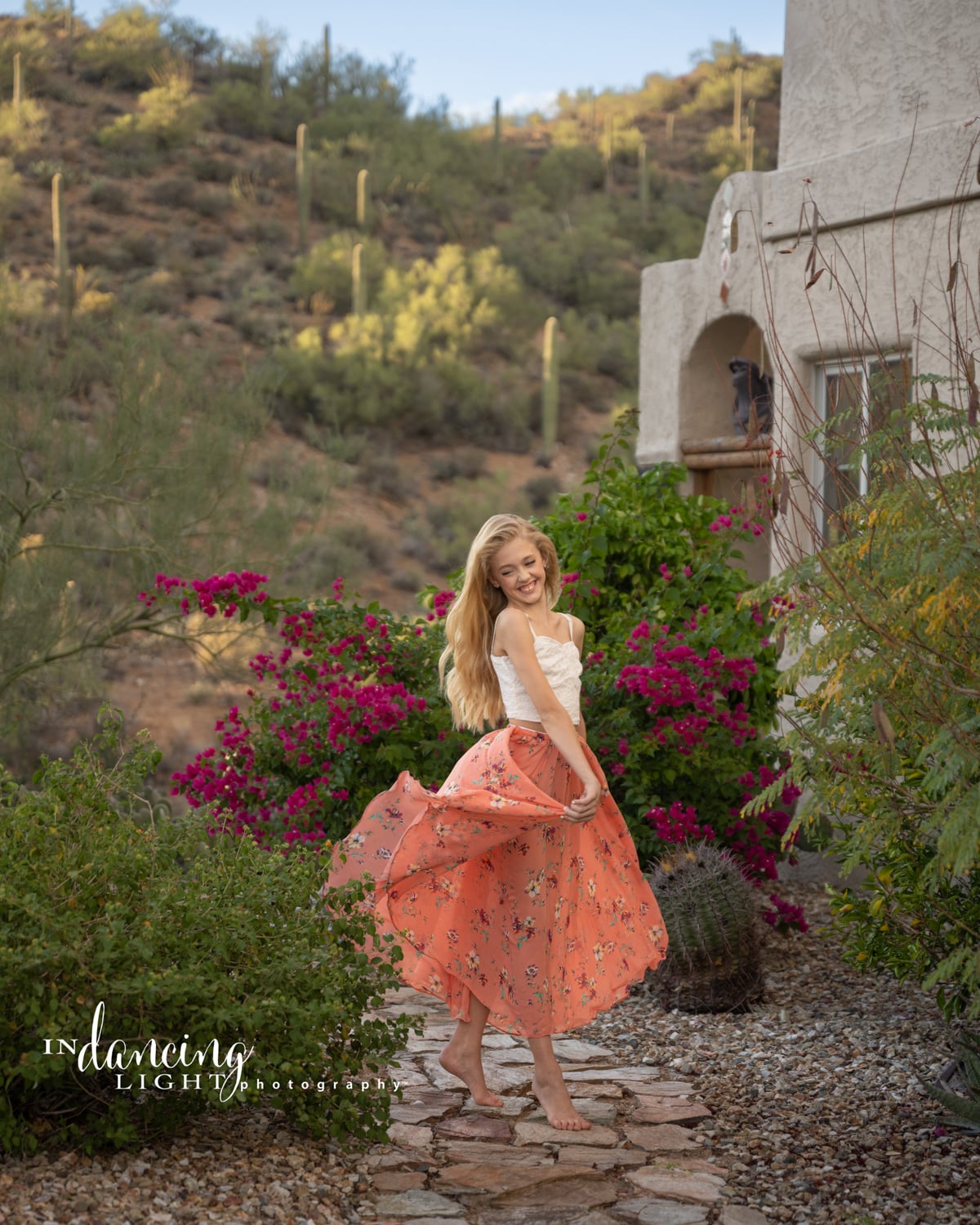 A young girl wearing an orange skirt dances along a desert pathway