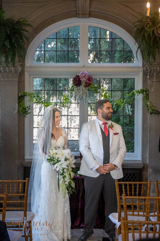 Bride and groom standing in front of a window in Indianapolis Laurel Hall. The bride holds her bouquet.