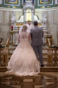 Wedding couple stand facing the alter during the ceremony in SS. Peter & Paul Cathedral chapel in Indianapolis
